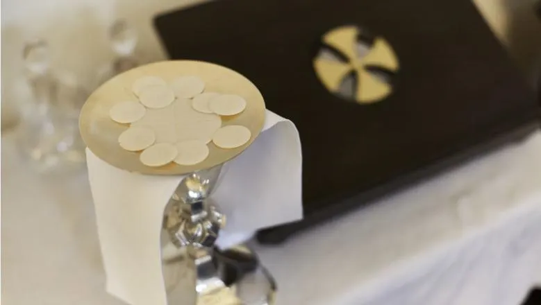 Communion wafers and silver chalice on clothed altar