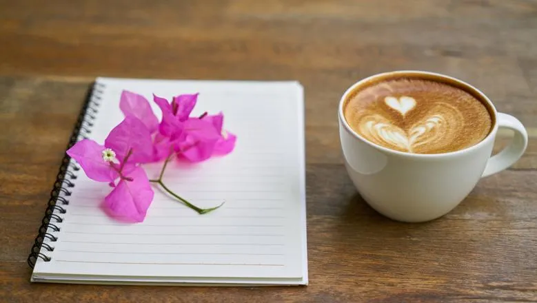 A notebook, flower sprig and coffee on a wooden table