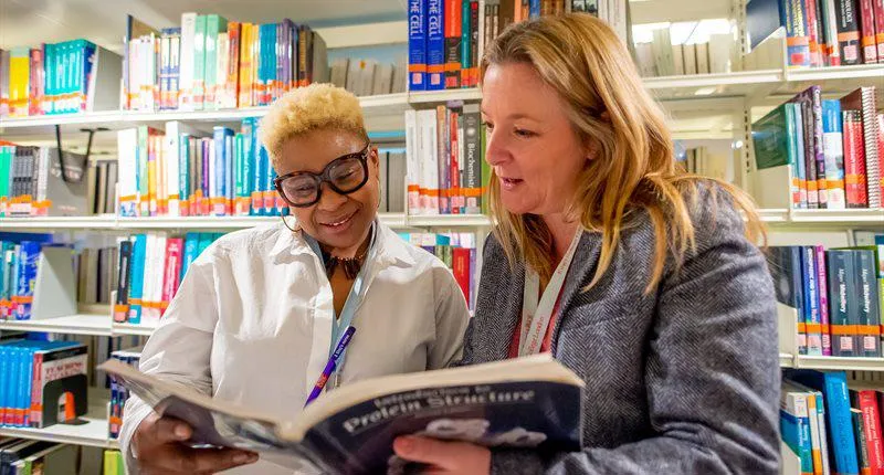 2 women reading a book in the library.