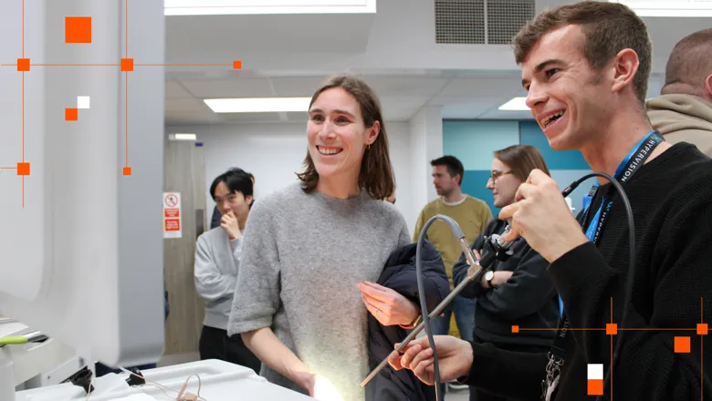 Two people staring a screen smiling, one is holding a medical device