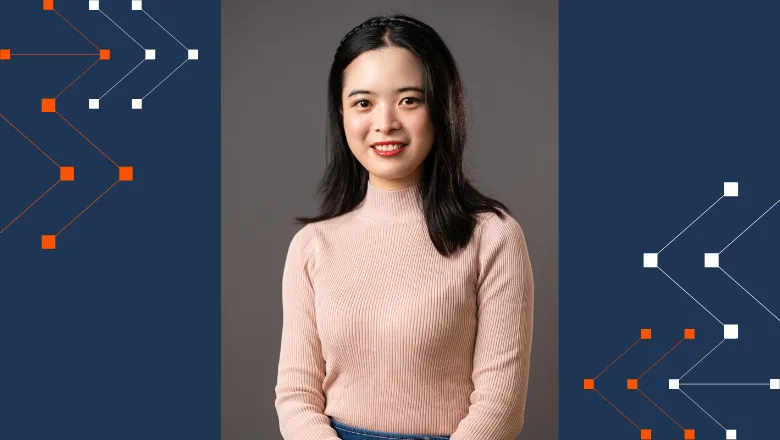 Jie Tang smiling and posing for a picture in front of a grey background