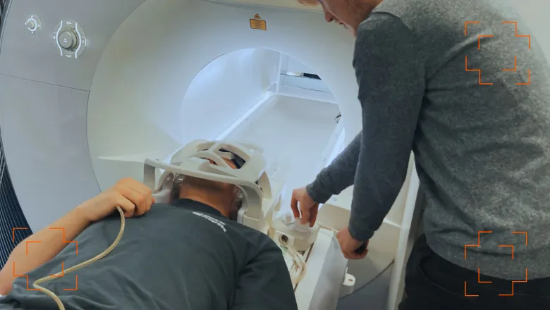 Man with the MR MinMo, which looks like a white head and neck brace, going into to an MRI, with a man helping him.
