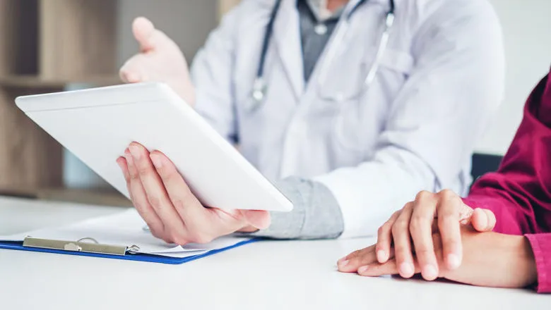Doctor consulting with patient presenting results on digital tablet tablet sitting at table