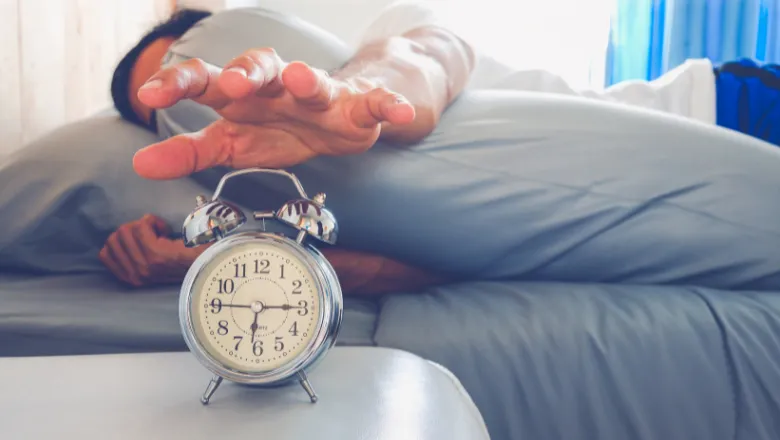 Person in bed reaches for an alarm clock on their side table