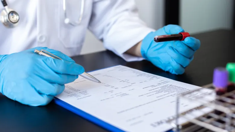 A doctor in blue gloves holding a blood sample and writing