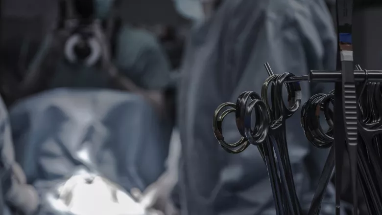 foreground shows surgical scissors, blurry background shows surgical team during operation
