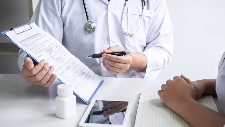 A doctor in a white coat writes notes on a clipboard in a clinical setting