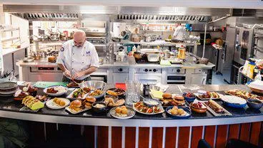 A commercial kitchen, with a table of prepared dishes including burgers