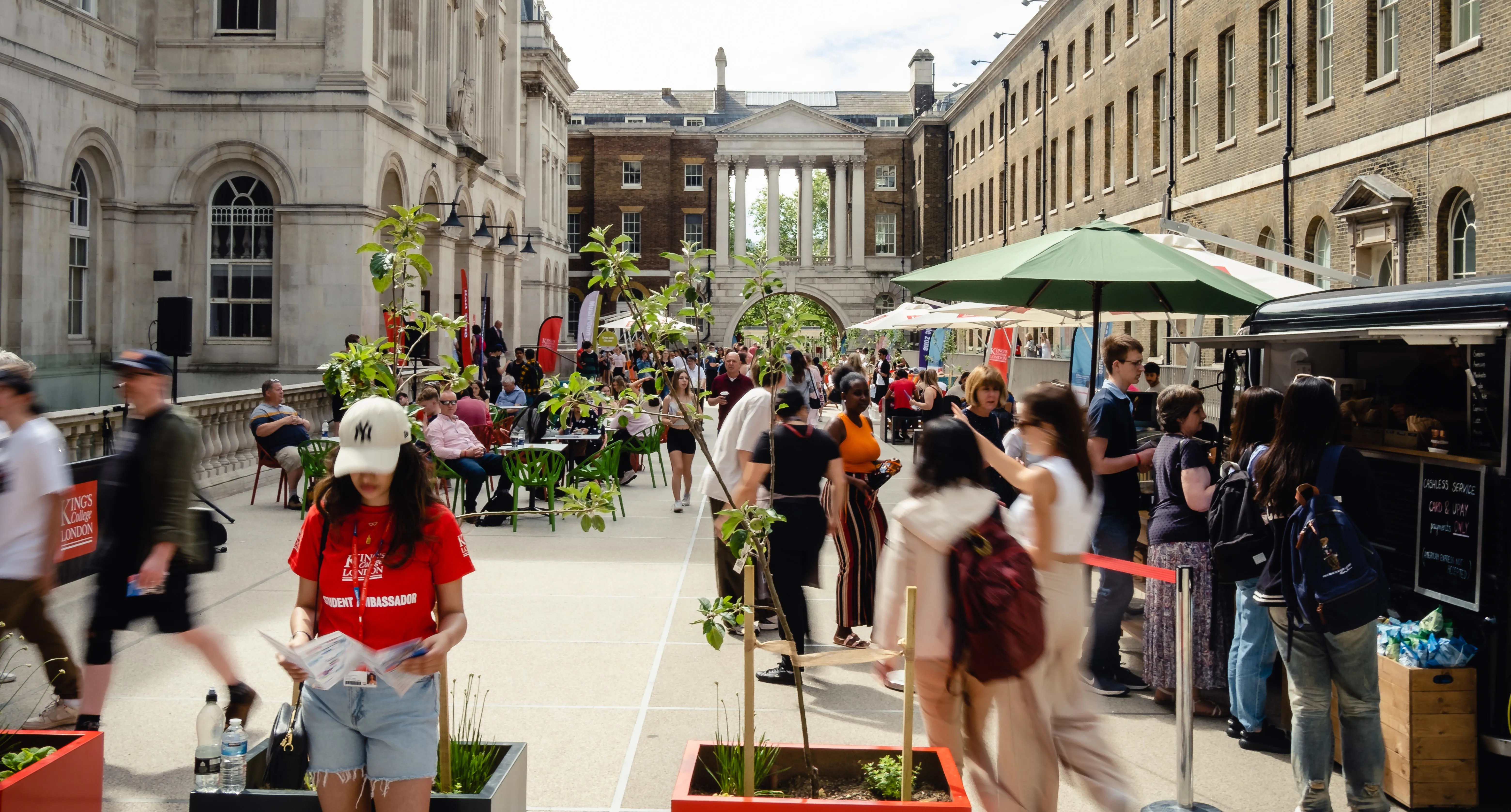 A quad courtyard, with people queuing at a van selling coffee, and chatting in conversation