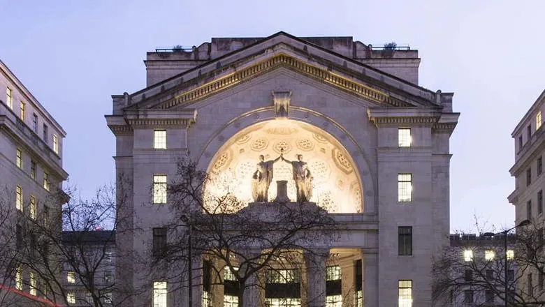 Top half of Bush House at night, with the statues at the north entrance lit up.