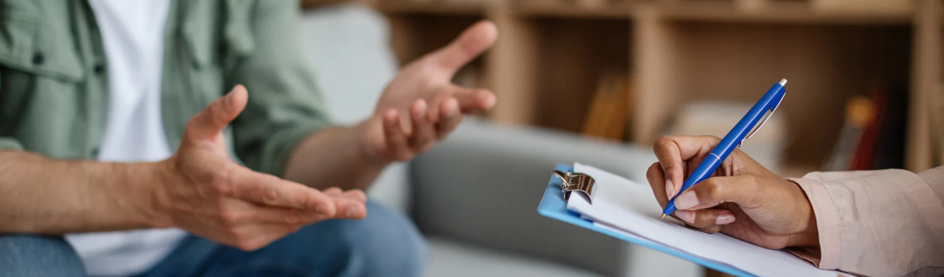 Close up of the hands of a therapy session - someone talking and someone writing notes 