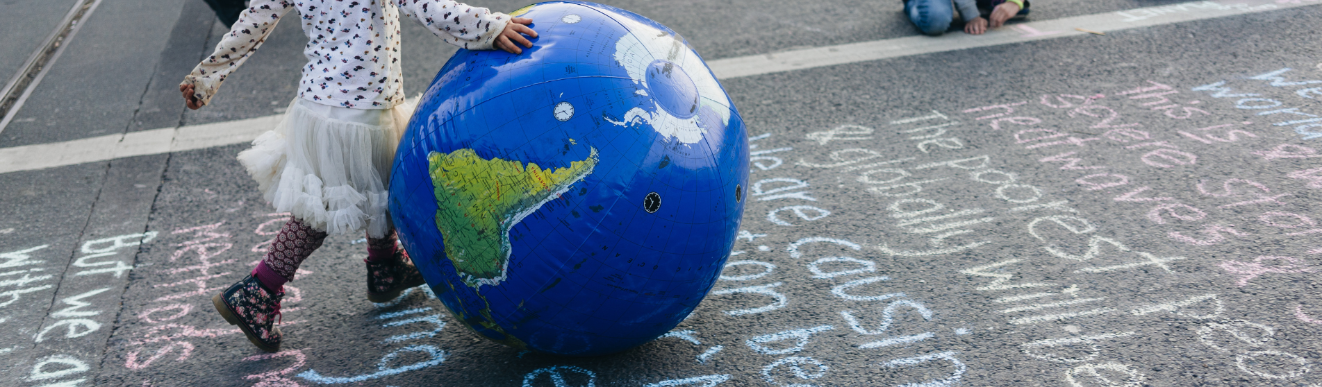 young child in starry long sleeve top and tutu rolls an inflatable globe along a pavement inscribed with climate facts