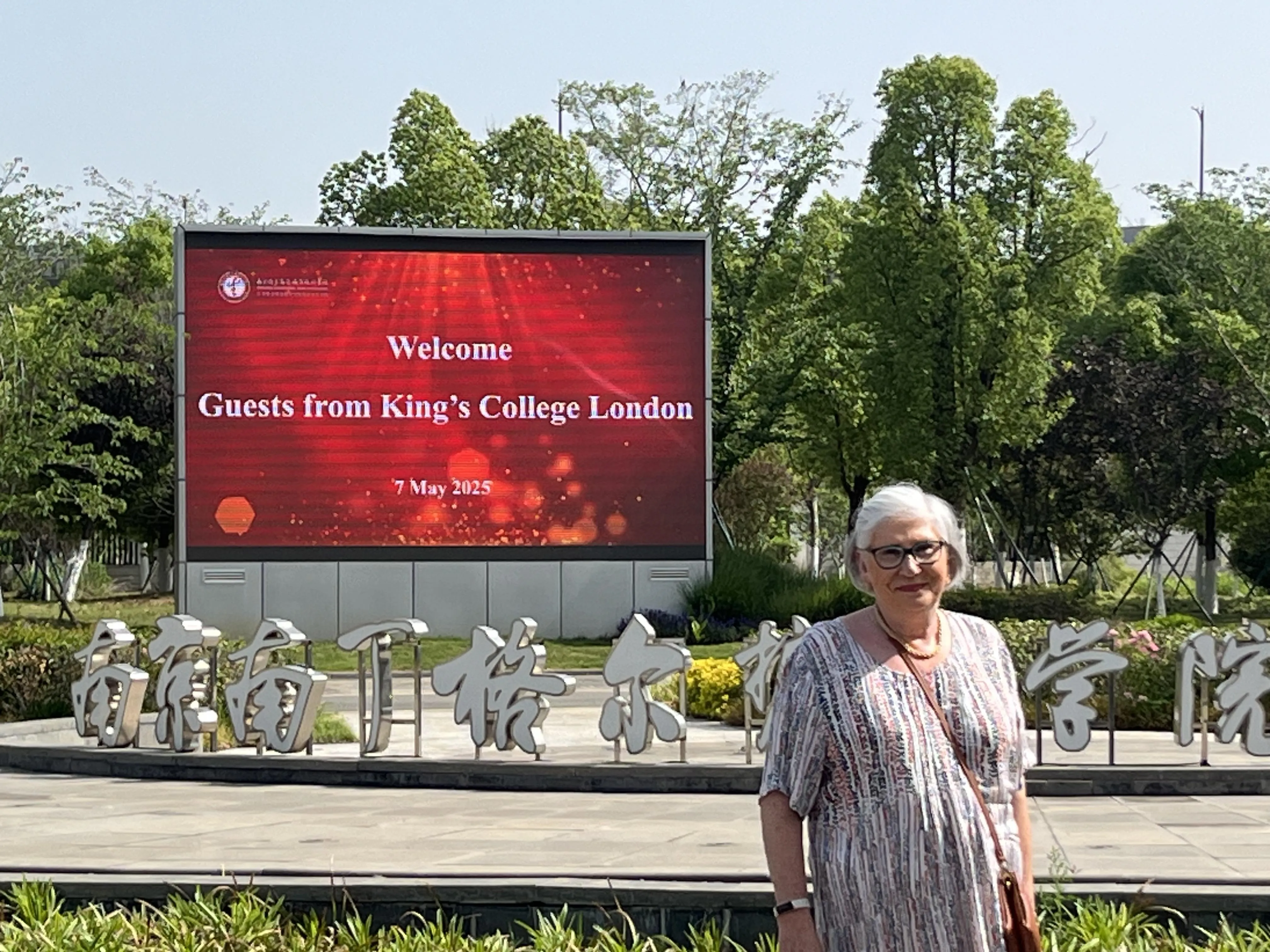 A woman stands in front of a sign reading 'Welcome Guests from King's College London, 7 May 2025'