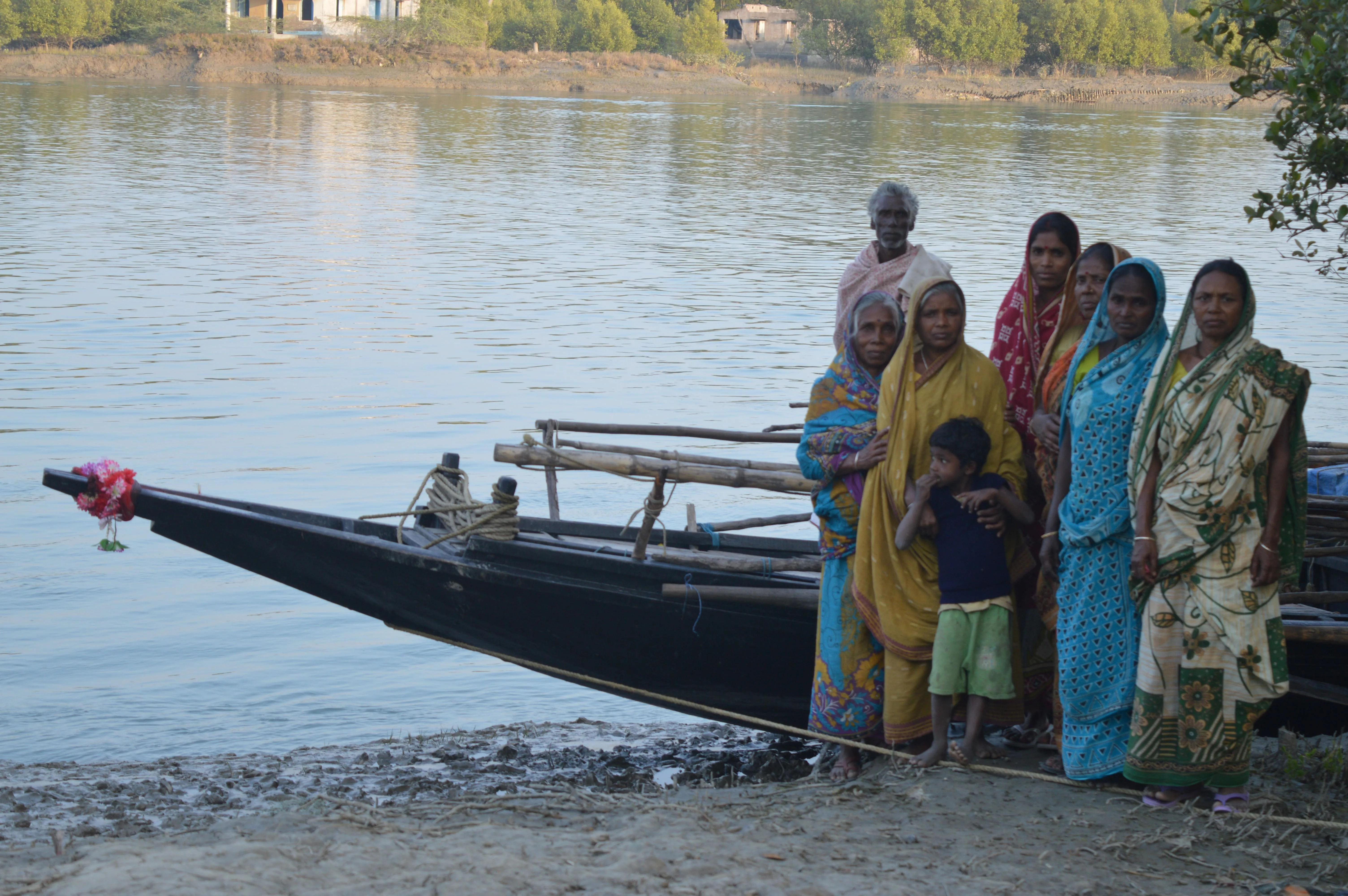 A group of tiger widows standing in front of a boat and a tiger widower standing on the boat in Sundarbans.