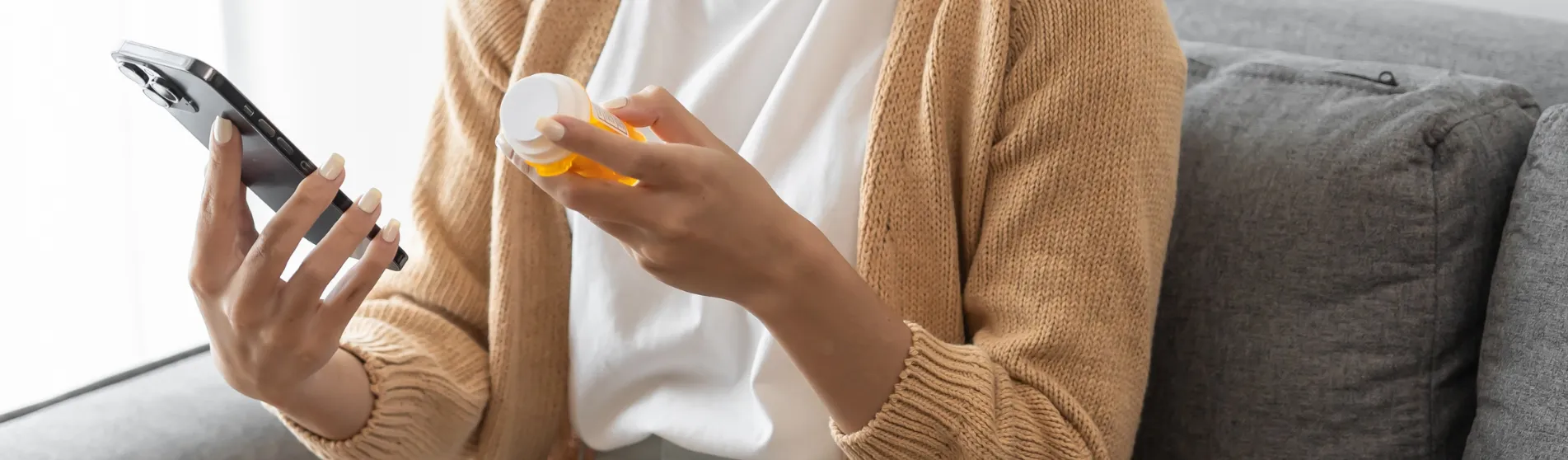A woman using a smartphone while holding a pill container in her other hand. Credit: Shutterstock