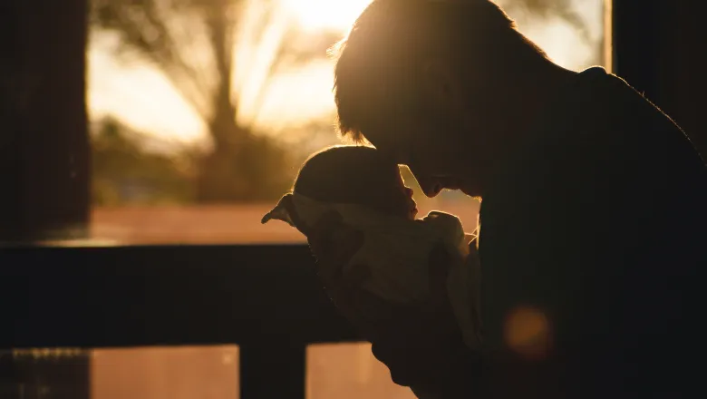 Father embracing infant child with sunset in background