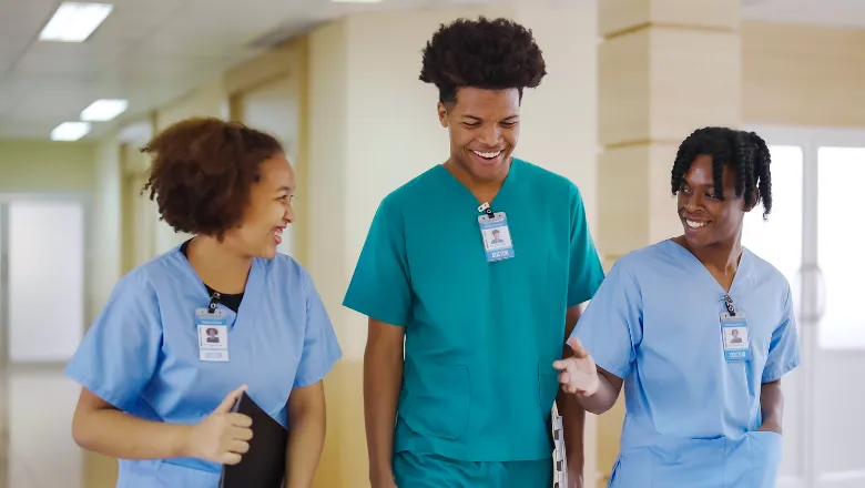 Three doctors walk through hospital corridors in their scrubs, smiling