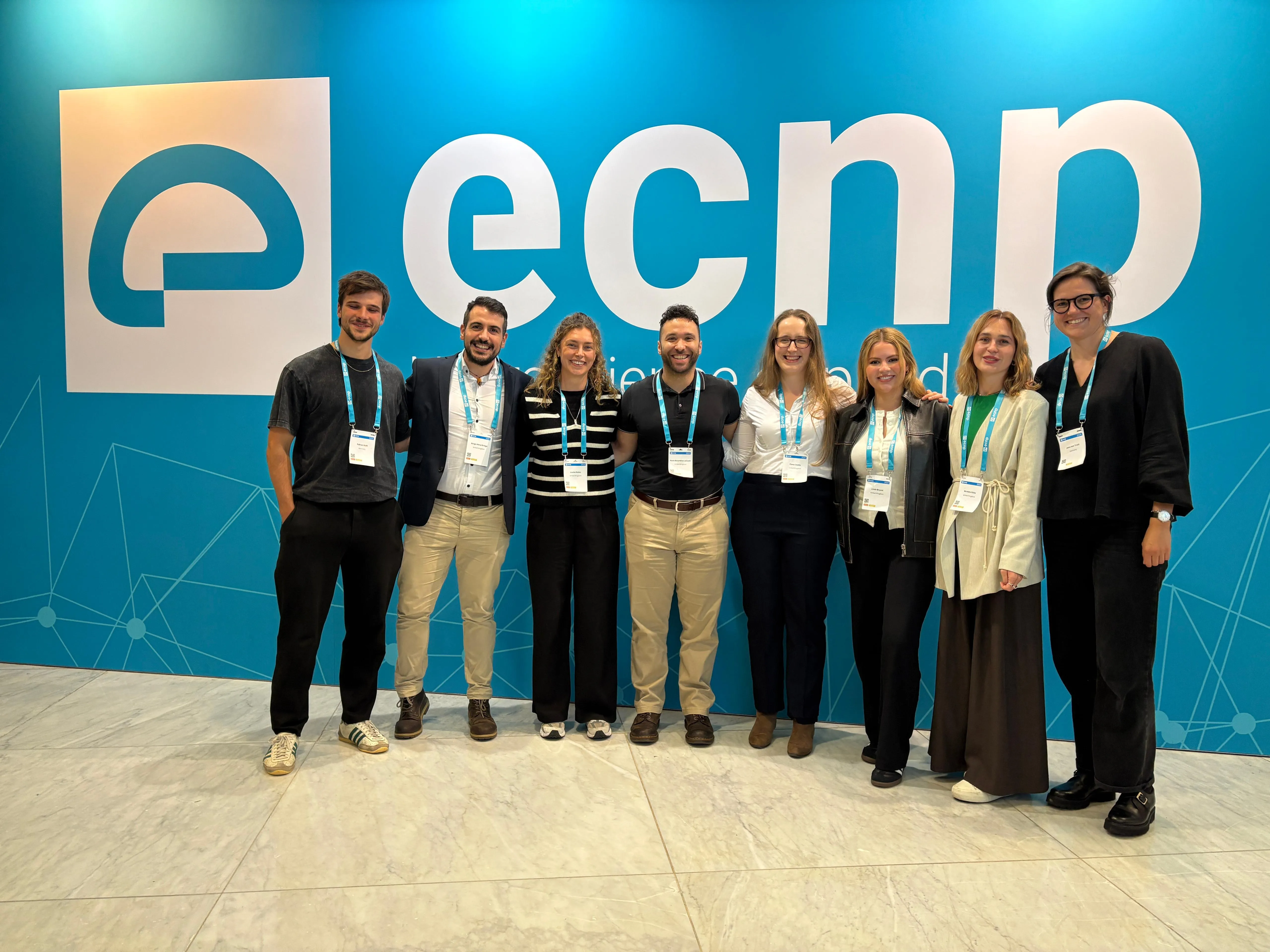 Group of eight conference attendees posing in front of a large ECNP logo wall.