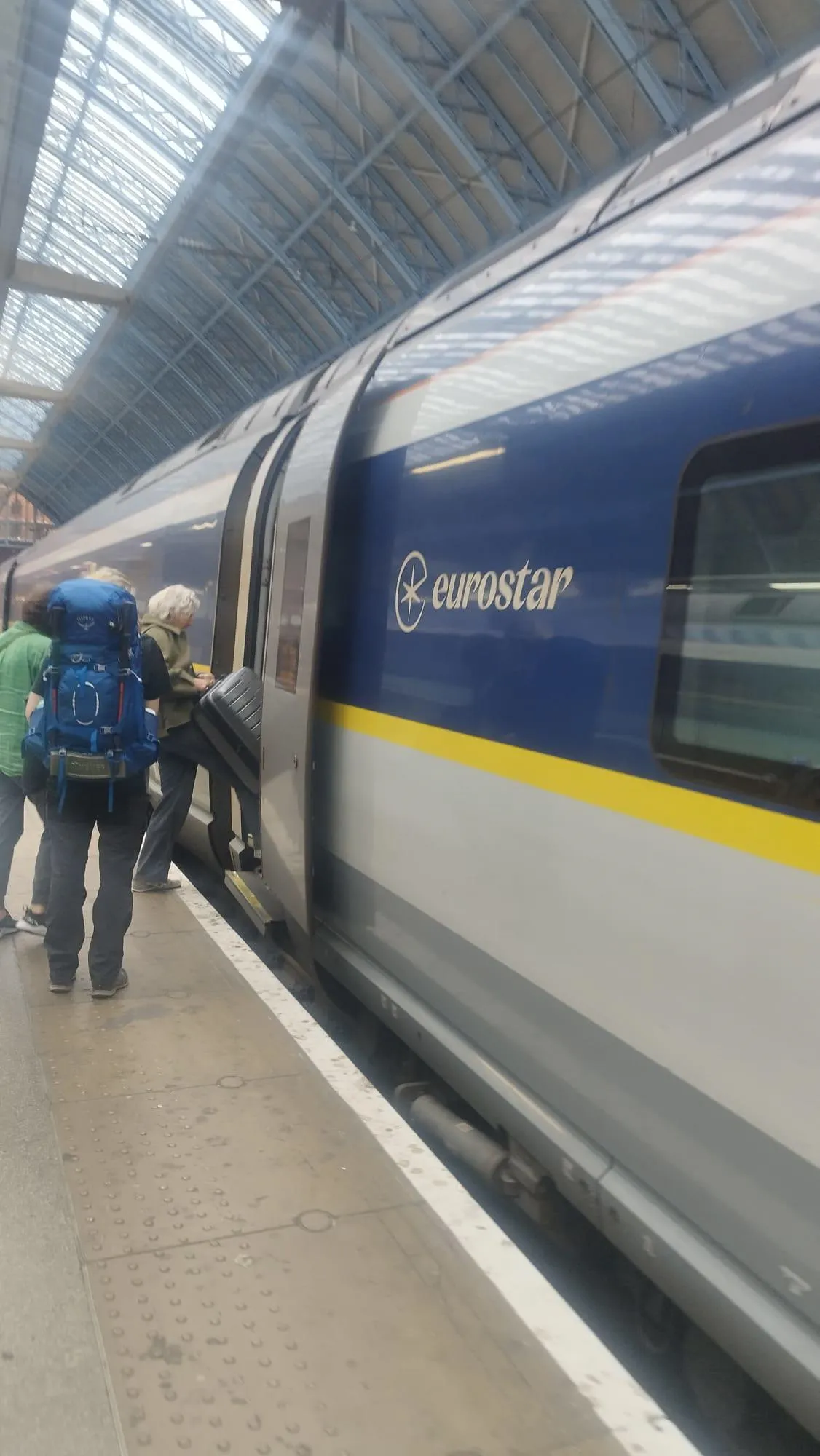 People boarding a blue and yellow Eurostar train at a covered station platform