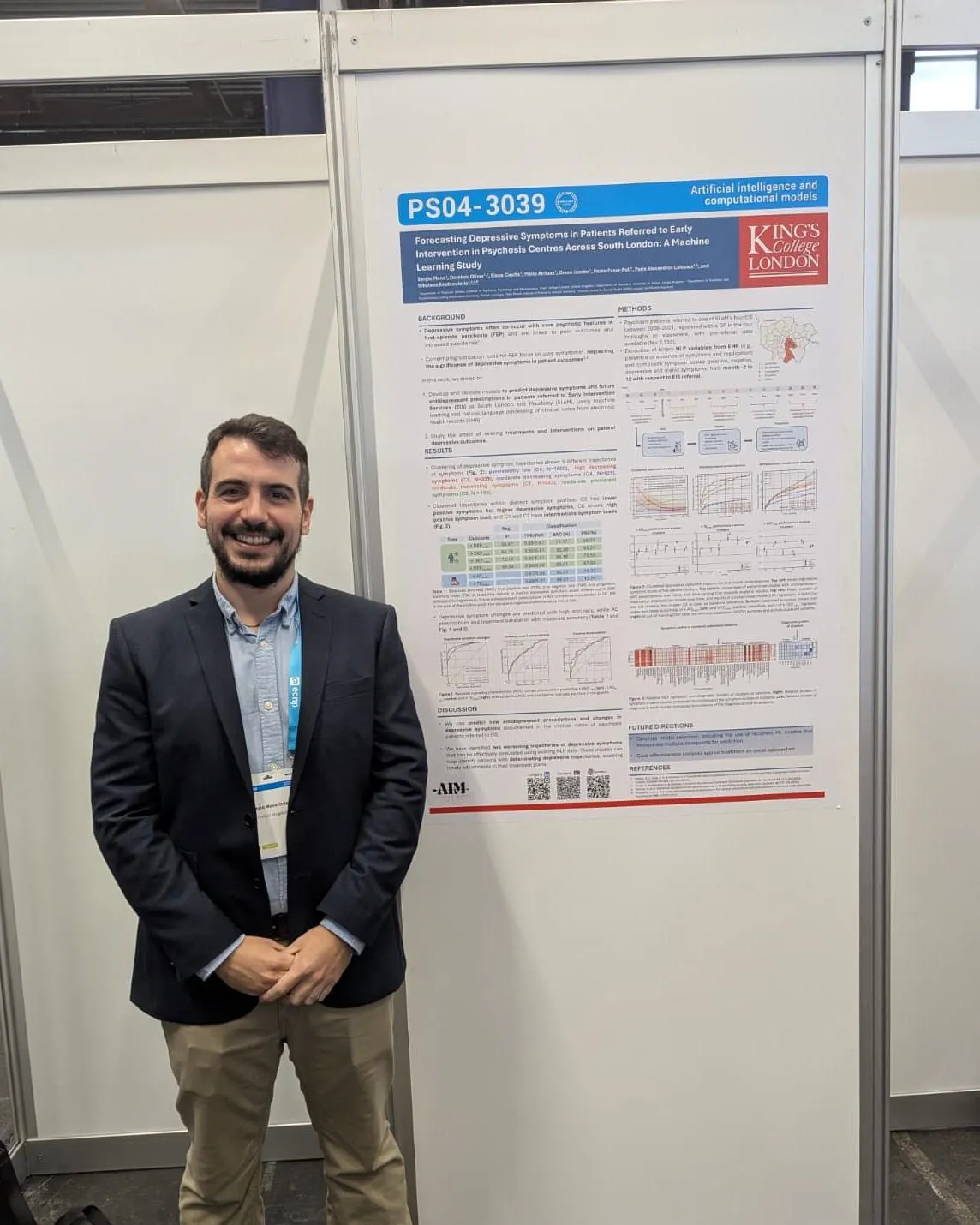 A man smiling while standing in front of a scientific poster at a conference