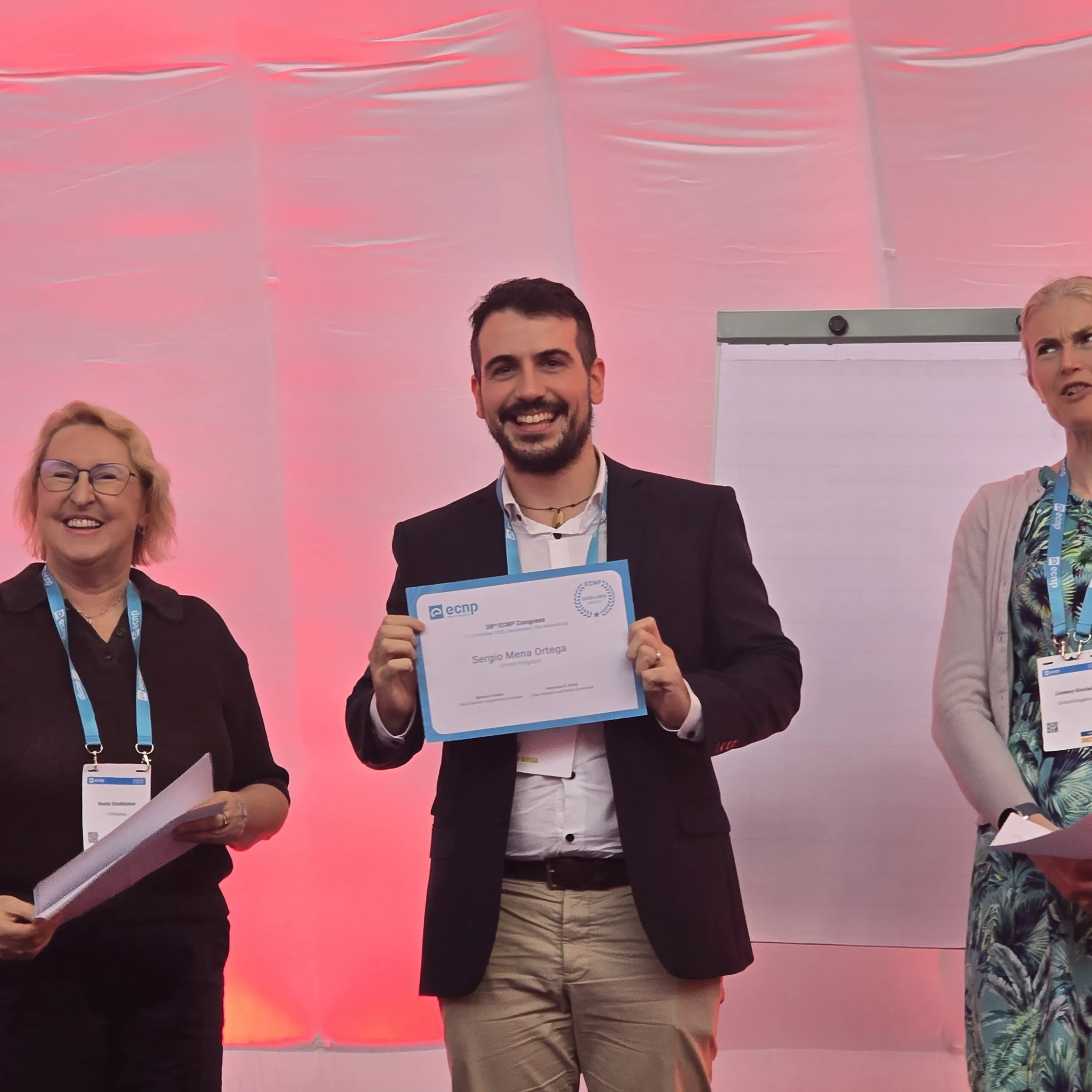 A man holding a certificate on stage between two other people at a conference event.