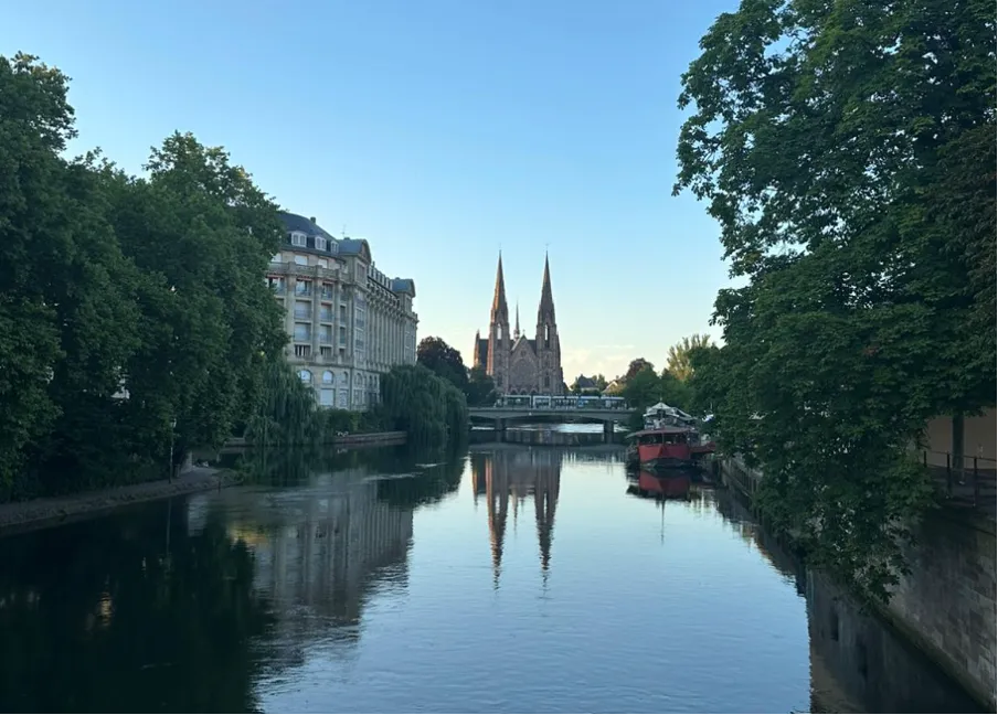Canal view in Strasbourg with trees, buildings, and a twin-spired cathedral in the distance
