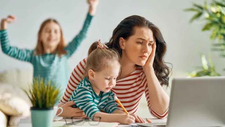 Woman looking stressed looking after two children at a laptop