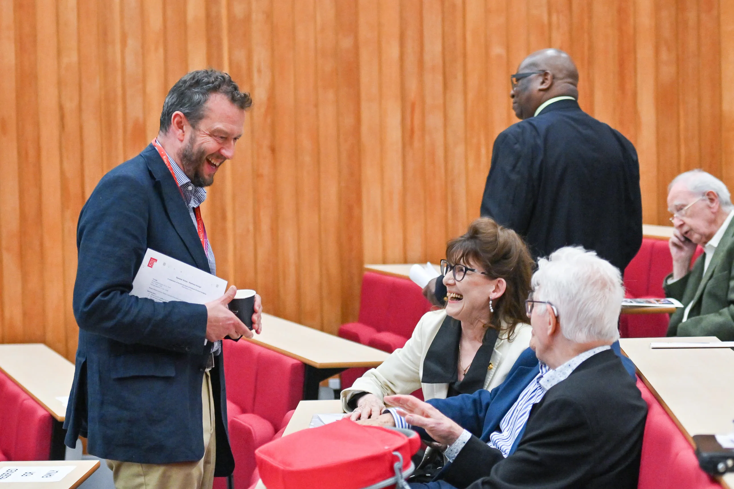 A man stood talking to two people seated in a lecture theatre
