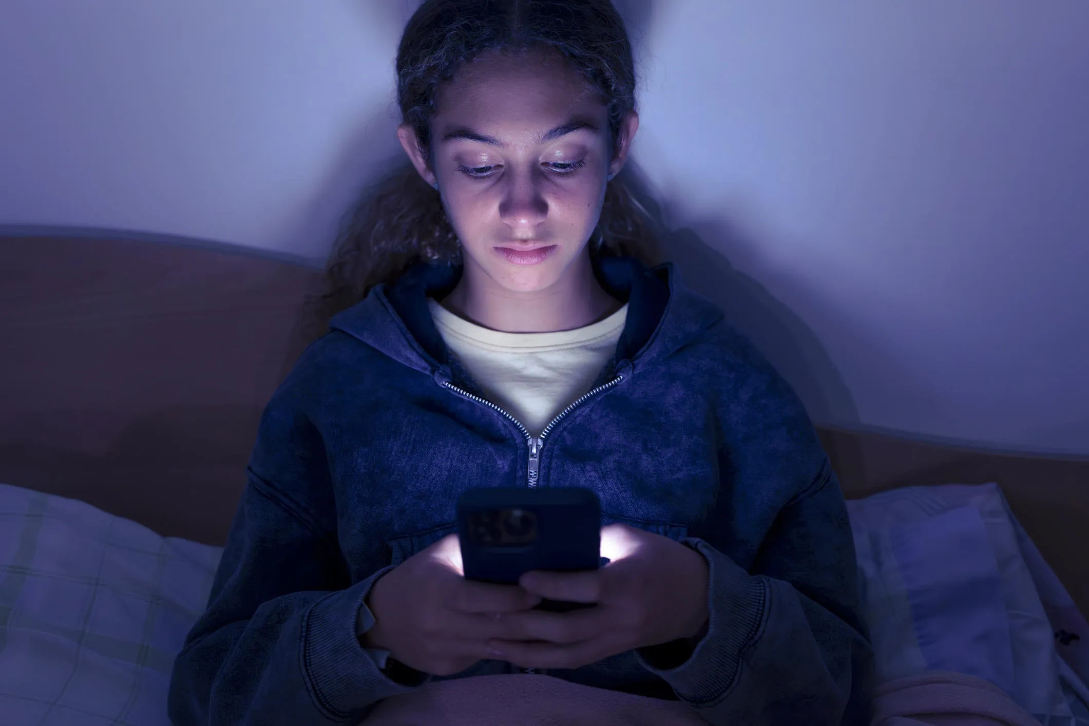 Teenage girl using a smartphone sitting in bed late at night
