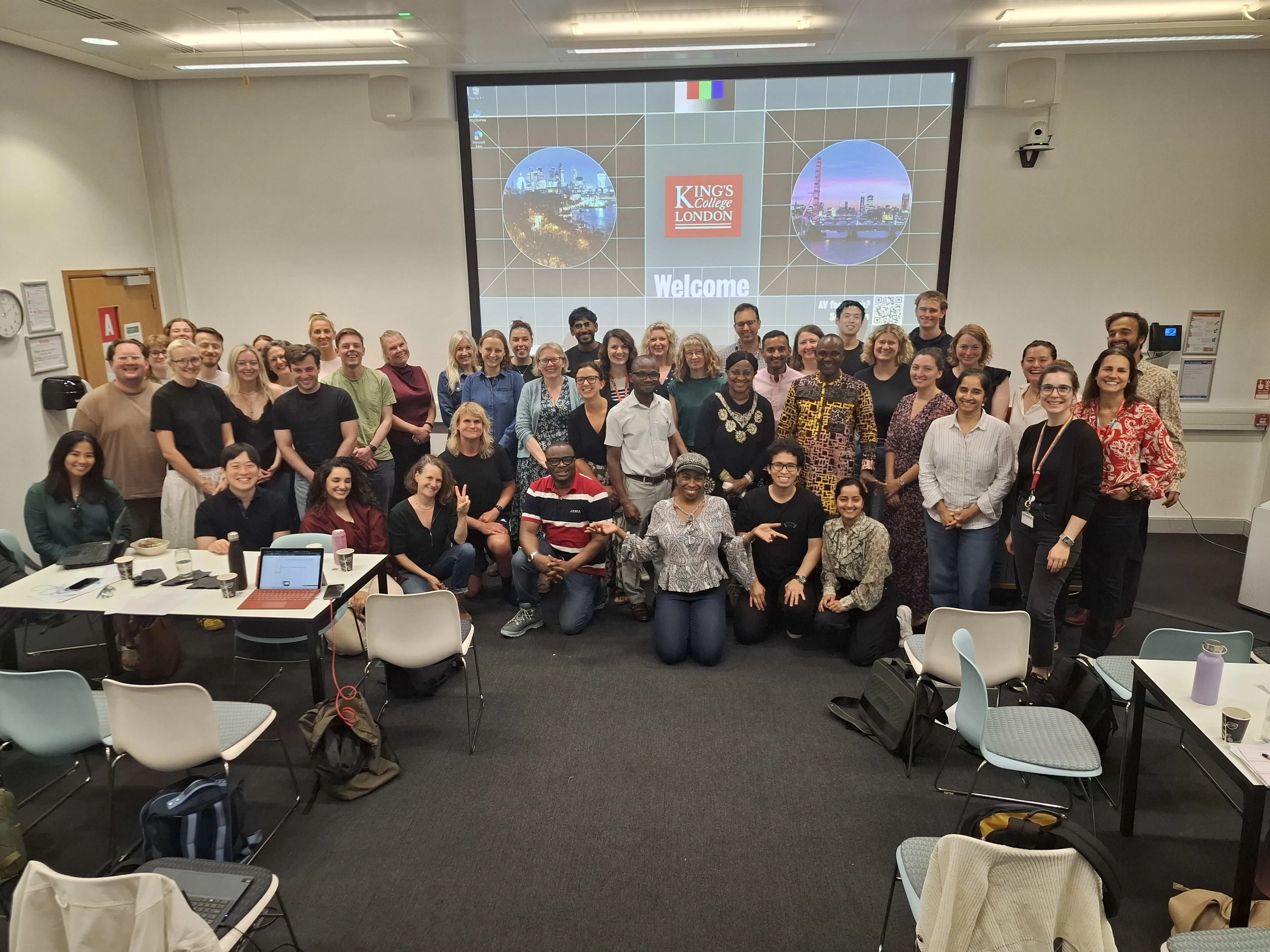 Diverse group of people posed in front of large screen in seminar room