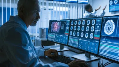 Man working on computer screens showing images of brain scans