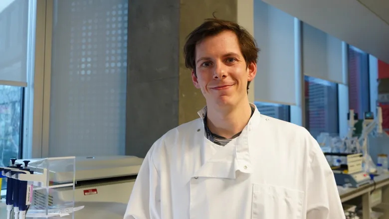 Dr Owen Gwydion James is in a white lab coat in the lab and smiling at the camera