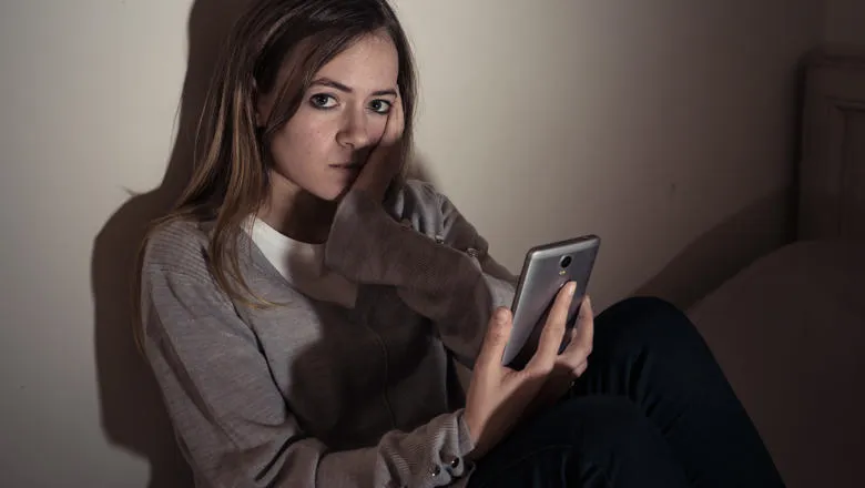 Woman looking sad holding a mobile phone in a darkened room