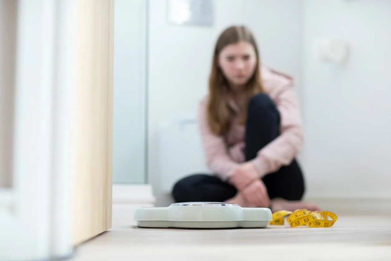 Girl sitting on a bathroom floor looking at weighing scales