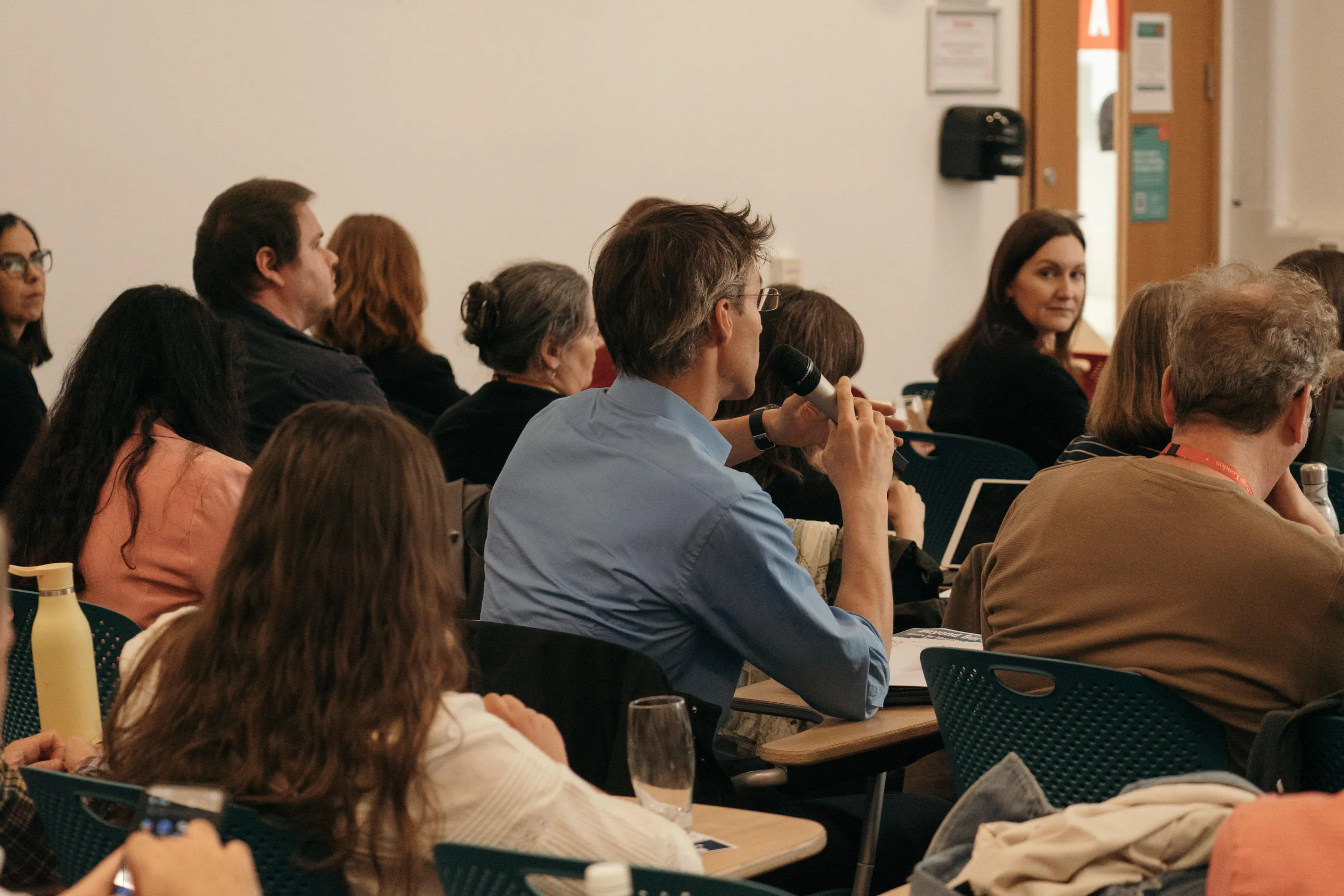 conference audience photographed from behind. Male audience member is holding a microphone