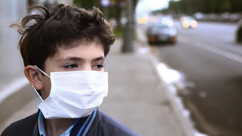 Young boy wearing a face covering next to a busy road
