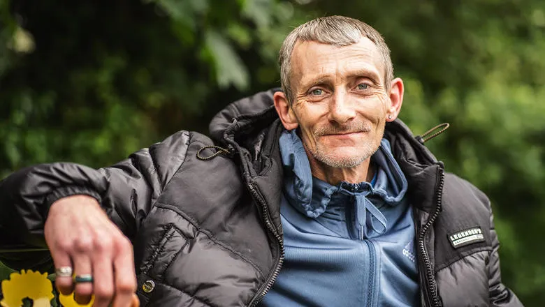 Man seated on bench, looking at camera and wearing multiple clothing layers
