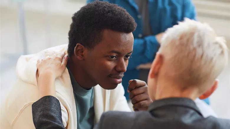 Young man looking face to face with another person who has their hand on his shoulder