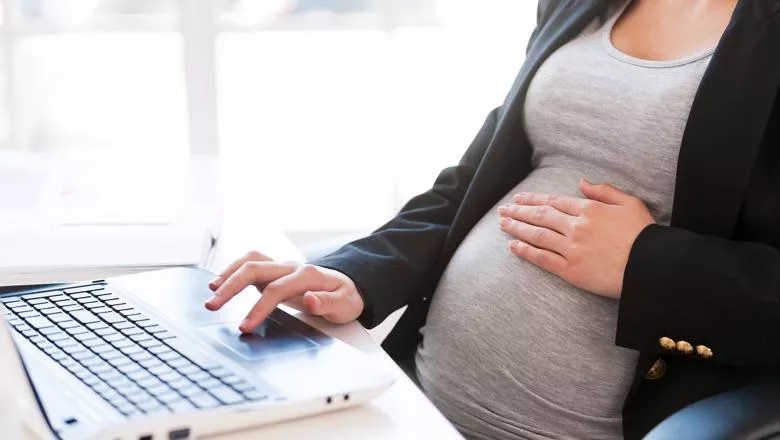Pregnant woman working on a laptop with a hand on her stomach