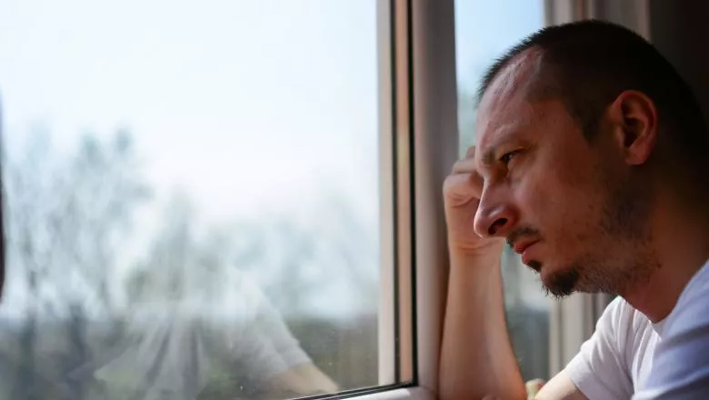 Middle aged man looking out a window looking depressed