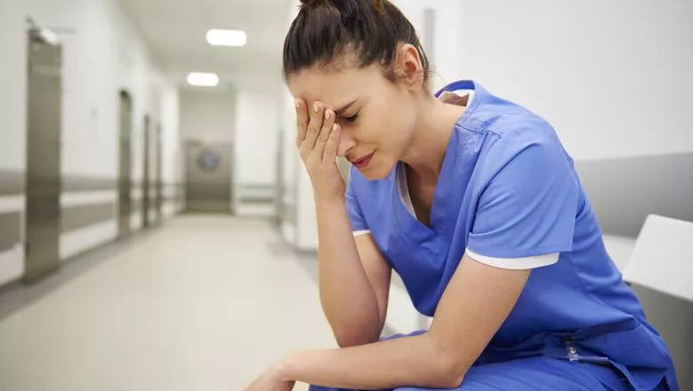 Female healthcare worker sat looking pained with her head on her hand