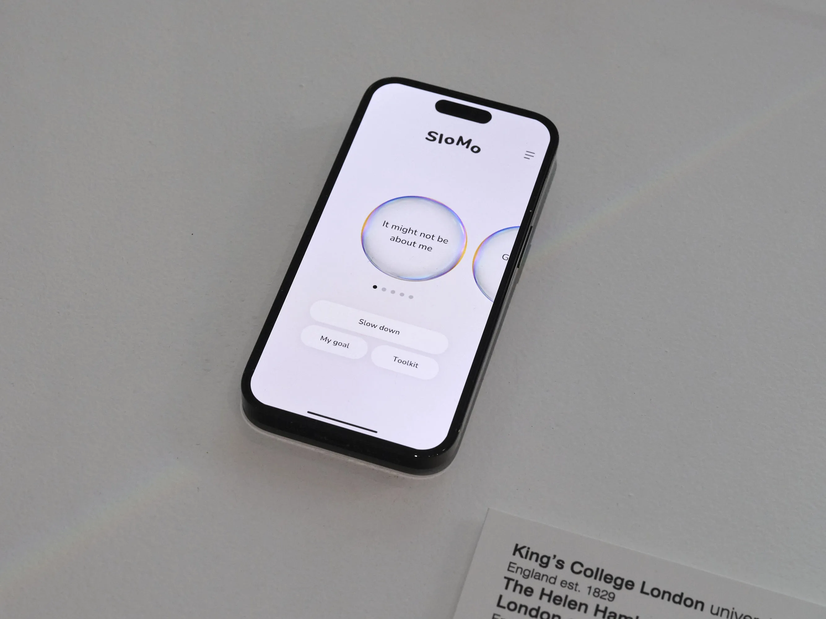 iPhone on white table with SloMo app open. Bubble on-screen contains text "it might not be about me"