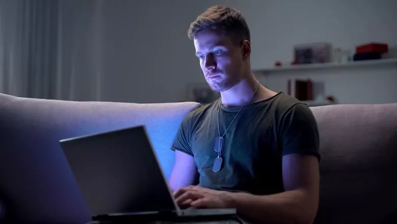 Young military man sat on a sofa looking at a laptop