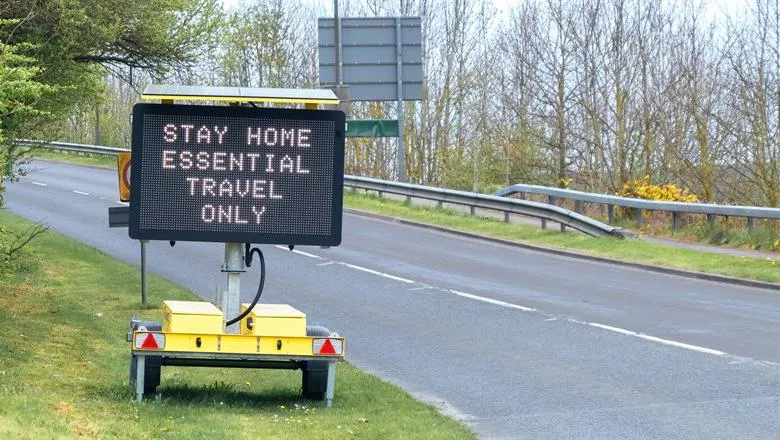 Digital sign on the side of an empty road reading 'stay home, essential travel only'