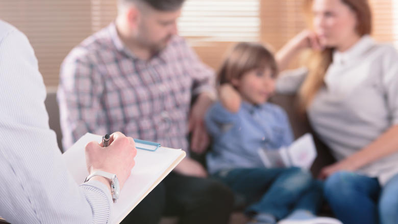 Blurred image of two parents sat on a sofa with a child opposite someone holding a clipboard