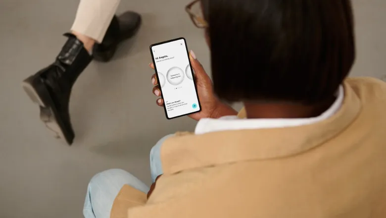 Person is shown holding a mobile phone with the SlowMo app open. Another person is shown walking past them. The top of the screen displays the text 