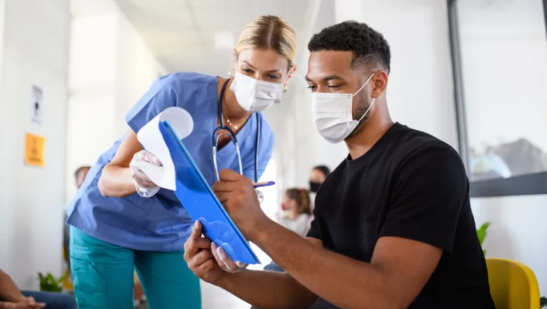 Doctor and patient wearing face masks looking at a clipboard together