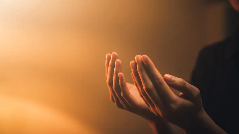 Hands praying against an orange background