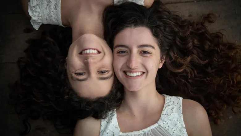 Two twin women lying on the floor smiling at the camera.