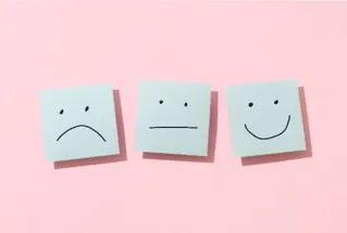 Pink background with three white squares. Left square has a simple frown face, middle square has simple ambivalent face, right square has simple smiley face.